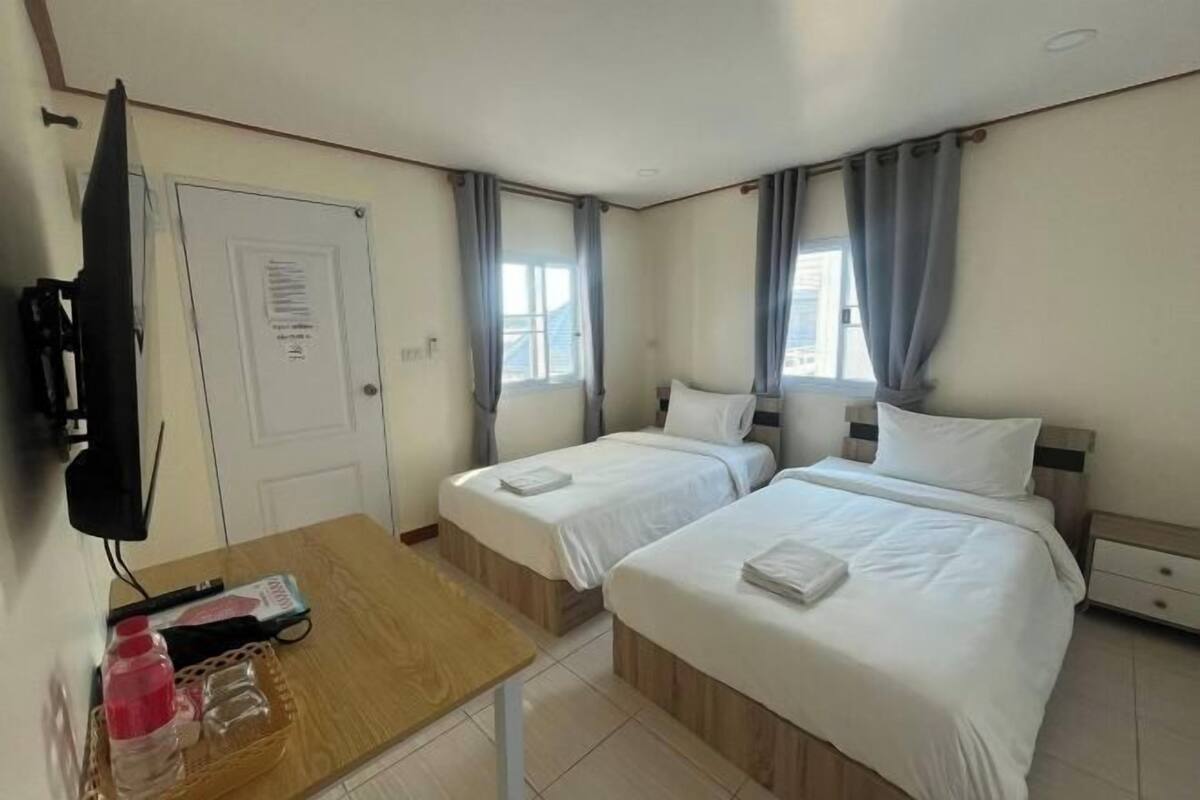 Ett hotellrum med två sängar, ett skrivbord med en tv och ett fönster med gardiner.
