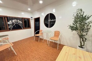 Una habitación con piso de madera, una mesa redonda, dos sillas, una planta en maceta y un reloj de pared.