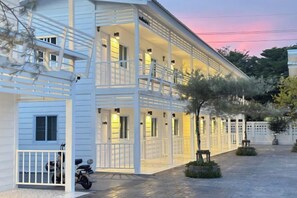 Un bâtiment blanc doté d’un balcon, une moto garée devant et une allée pavée.