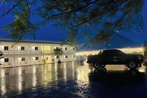 A building with a covered outdoor area, a parked SUV, and a tree with lights. - Duangdeerojehouse (Chon Buri)