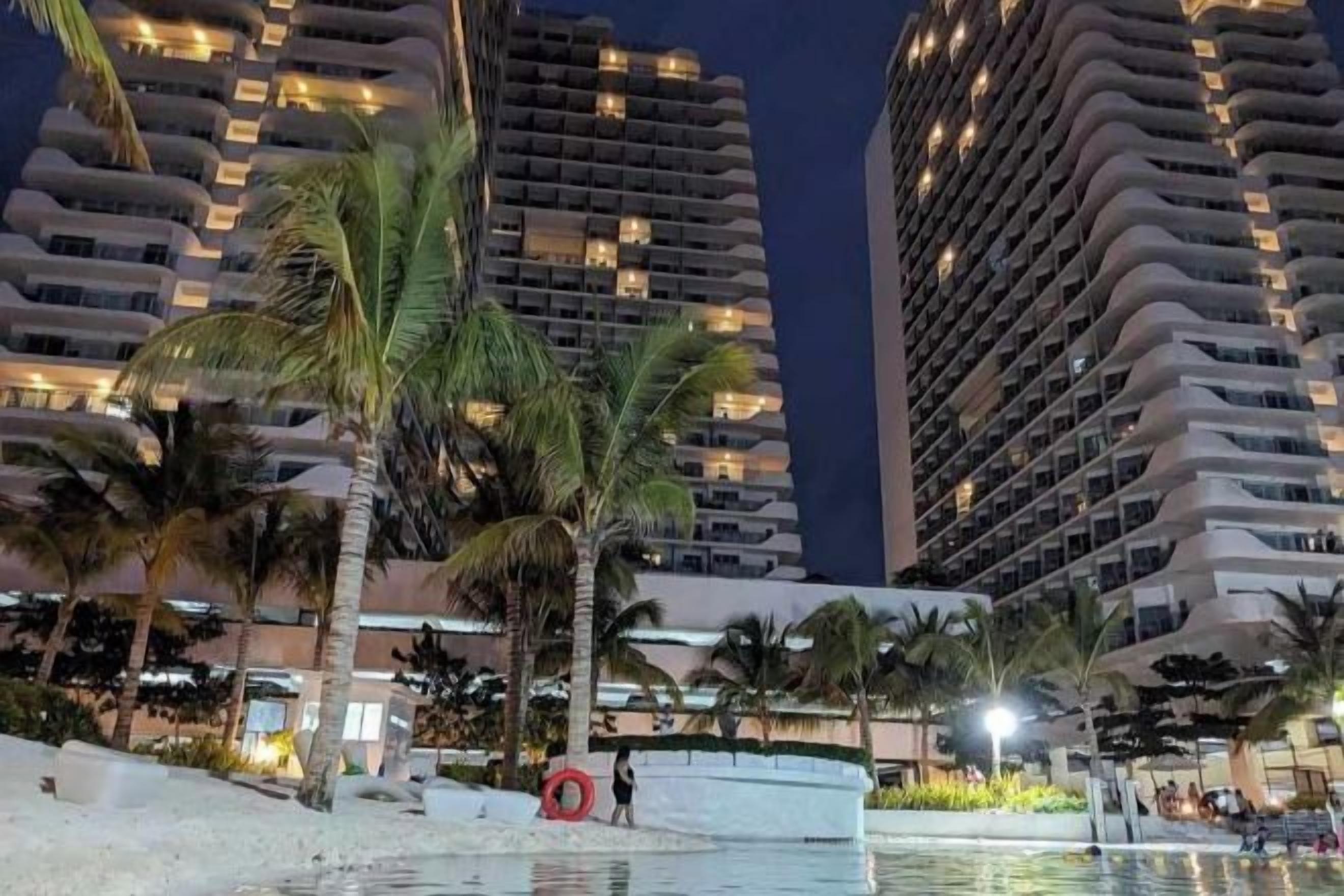 Un hotel di grattacielo con numerosi balconi, palme e area piscina.