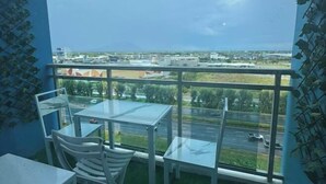 Un balcon doté d’une table et de chaises en verre, offrant une vue sur une rue et des immeubles.