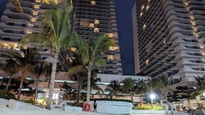 Un hôtel de grande hauteur doté de nombreux balcons, de palmiers et d’un espace piscine.