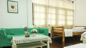 A room with a green sofa, a wooden chair, a small table with a checkered tablecloth, and a bed with a white mattress. - Deng Ba Hostel Bangkok (Bangkok)