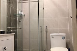 A bathroom with a glass shower enclosure, a toilet, and a white cabinet with a sink.