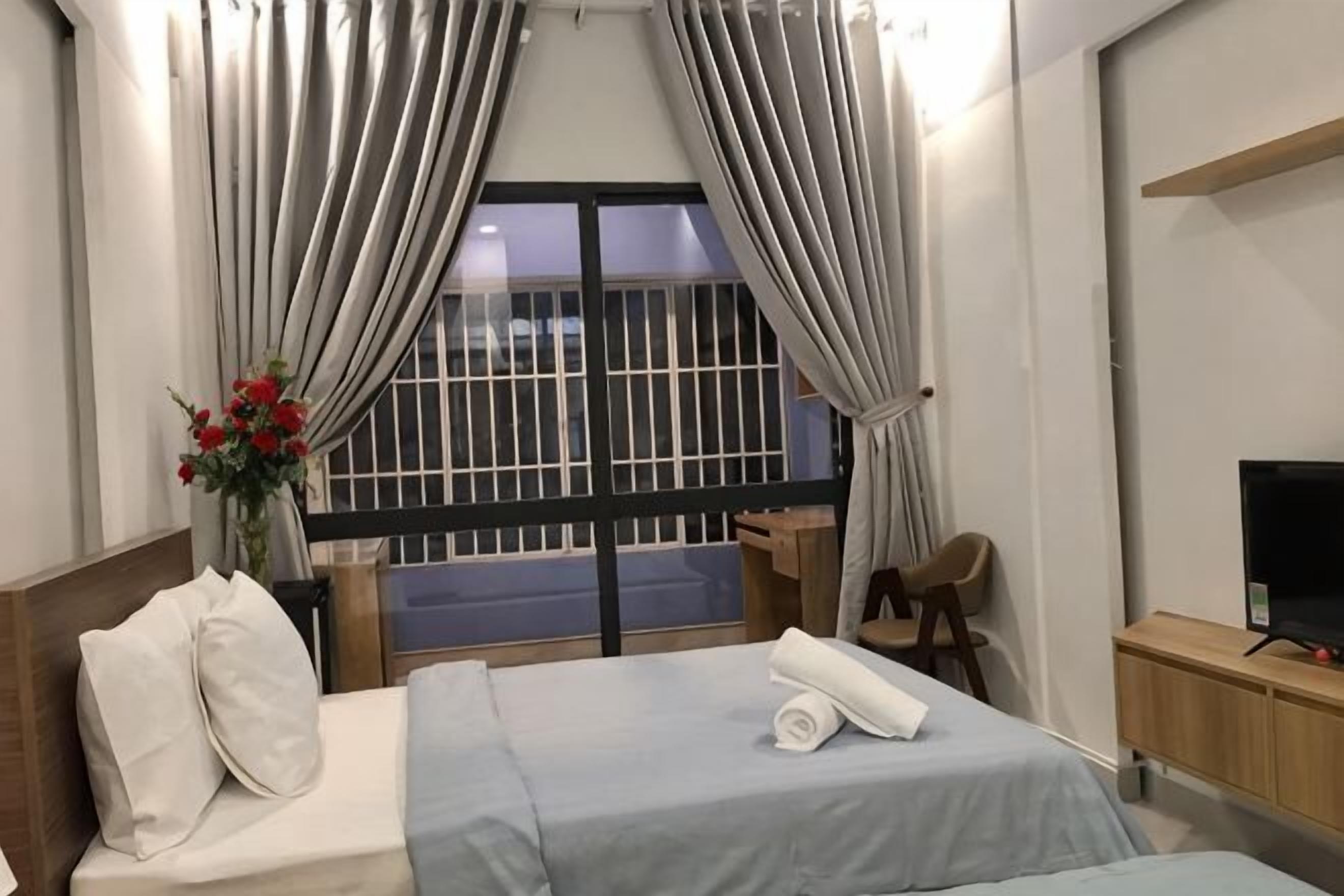 A hotel room with a bed, a TV, a desk, and a window with curtains.