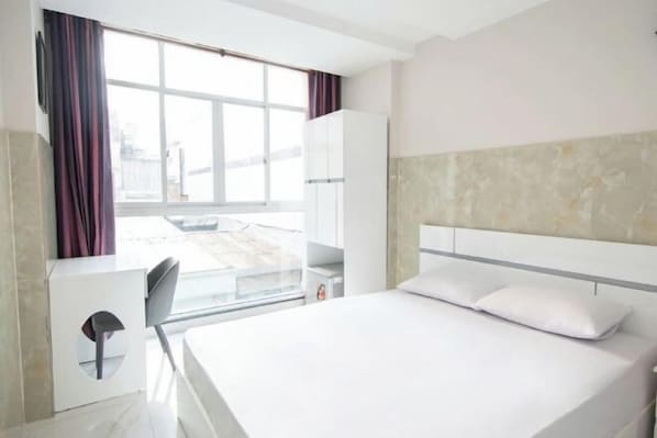 A hotel room with a bed, a desk, and a window.