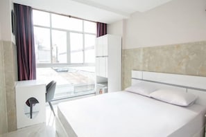 A hotel room with a bed, a desk, and a window.