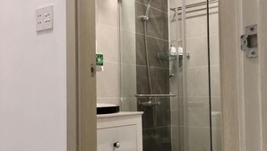 A bathroom with a glass shower enclosure, a white sink, and a cabinet with drawers.