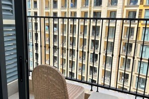 A balcony with a wicker chair, a black metal railing, and a view of a multi-story building with balconies. - Seaside Fireworks Apartment Free Pool & Gym (Phu Quoc Island)