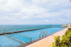 A swimming pool with a view of the sea, a glass barrier, and a tiled deck. - Seaside Fireworks Apartment Free Pool & Gym (Phu Quoc Island)