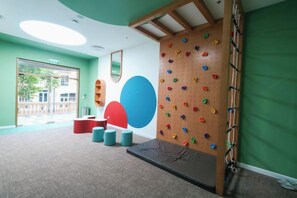 A room with a climbing wall, a large blue and red circular design on the wall, and a window with a view of the outside. - Seaside Fireworks Apartment Free Pool & Gym (Phu Quoc Island)