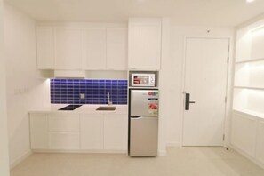 A compact kitchen with white cabinets, a stainless steel refrigerator, and a blue tiled backsplash.