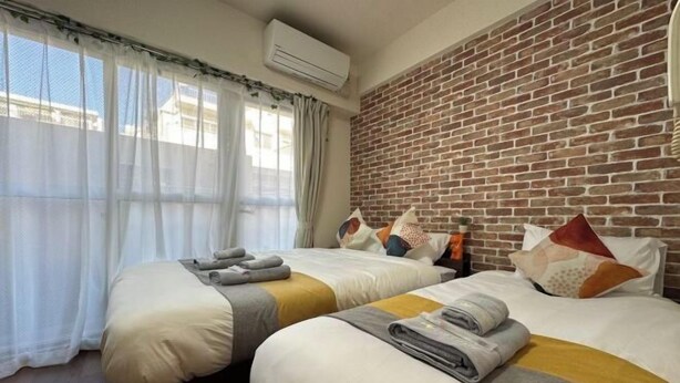 Une chambre d’hôtel avec deux lits, un mur en briques, un climatiseur et des rideaux en voile.