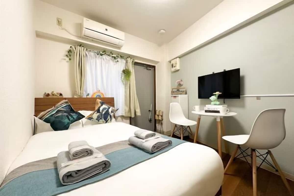 A hotel room with a bed, a desk, a chair, a TV, and an air conditioning unit.
