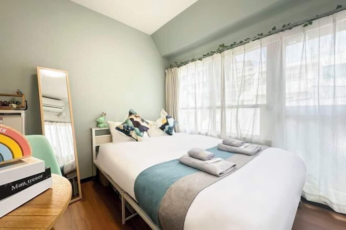 A hotel room with a bed, a bedside table, a mirror, a dresser, and a window with curtains.