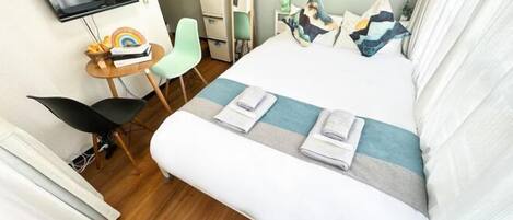 A hotel room with a bed, a desk, a chair, a television, and a small table with a rainbow toy.
