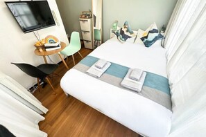 Habitación de hotel con cama, escritorio, silla, televisión y una pequeña mesa con un juguete de arcoíris.