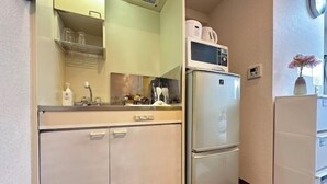 Une cuisine compacte équipée d’un réfrigérateur, d’un four à micro-ondes et d’une étagère contenant des ustensiles de cuisine.
