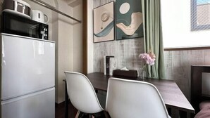 Une cuisine compacte équipée d’un réfrigérateur, d’un four à micro-ondes et d’une bouilloire, ainsi que d’une table à manger avec des chaises et de deux œuvres d’art abstraites accrochées au mur.