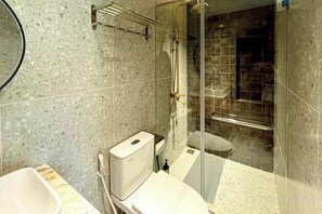 Une salle de bain comprenant des toilettes, un lavabo, une douche et un espace de douche séparé par une paroi en verre.
