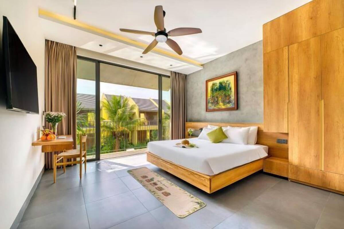 Een moderne slaapkamer met een groot bed, een bureau en uitzicht op palmbomen.