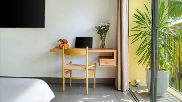 Een moderne hotelkamer met een houten bureau, een laptop, een stoel, een kleine plant en een groot raam met uitzicht op groen.
