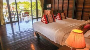 A hotel room with a large bed, a TV, and a balcony with chairs.