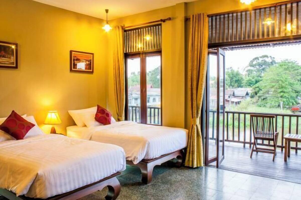 A hotel room with two beds, a balcony, and a view of the outdoors.