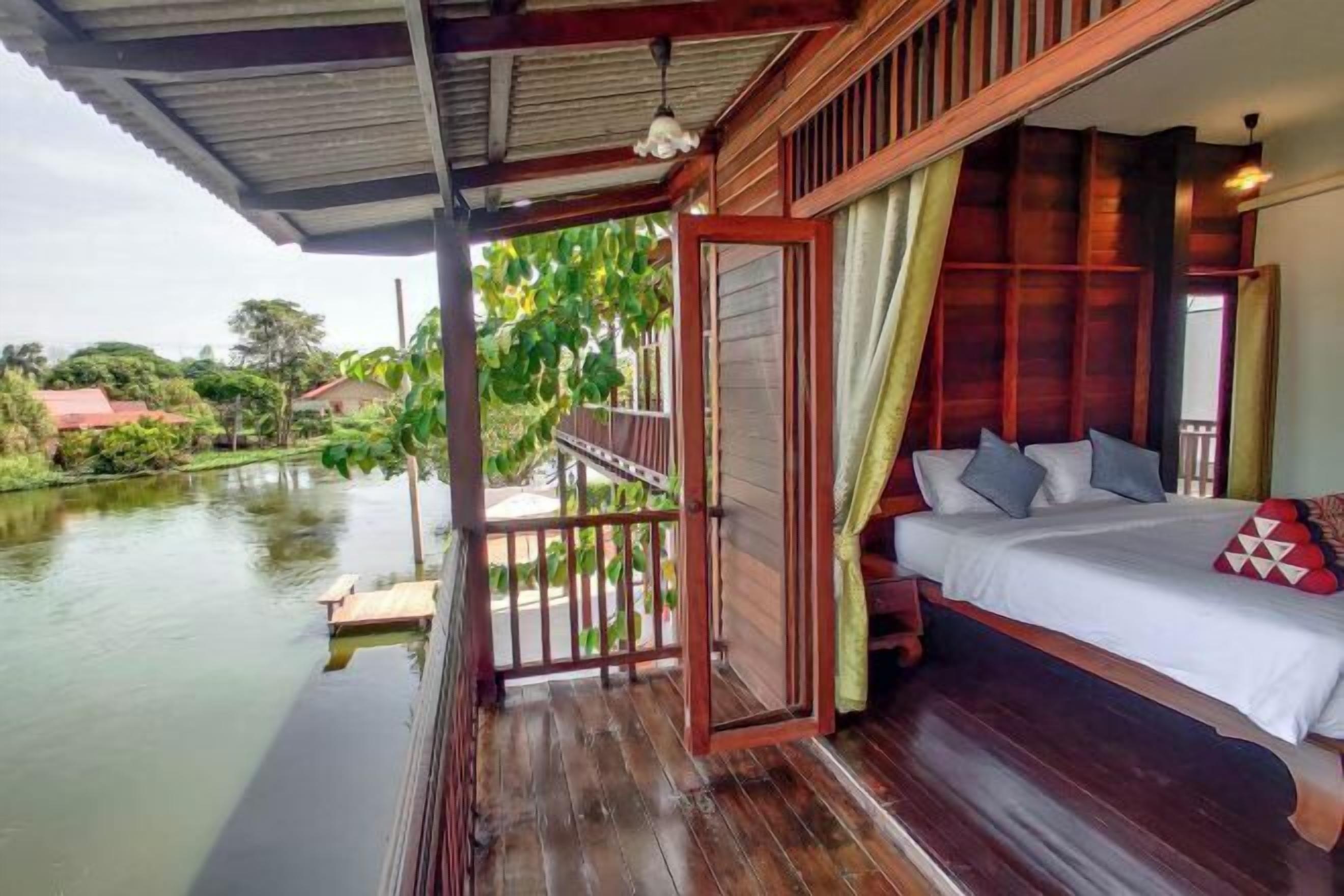 A wooden balcony with a bed, a view of a river, and a covered area with a railing.