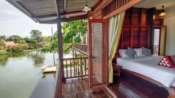 A wooden balcony with a bed, a view of a river, and a covered area with a railing.