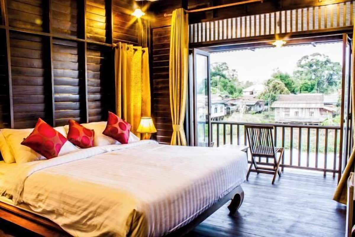 A bedroom with a large bed, a wooden headboard, a nightstand, a lamp, and a view of the outside through a balcony.