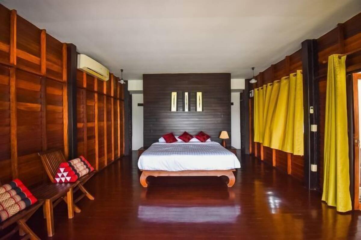 A room with a bed, wooden walls, a bench, and yellow curtains.