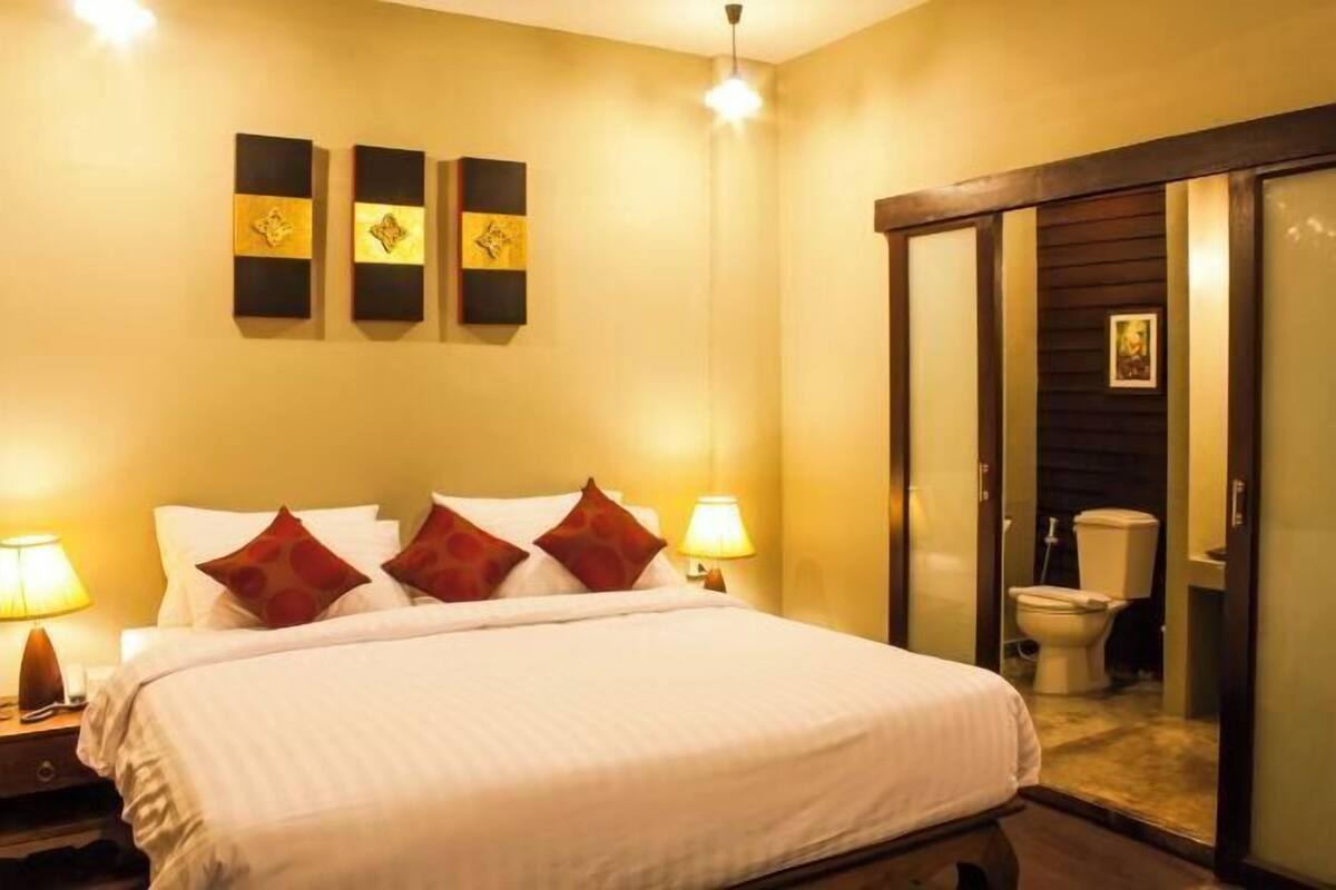 A hotel room with a bed, two bedside lamps, a nightstand, a wall-mounted artwork, and a sliding door leading to a bathroom.