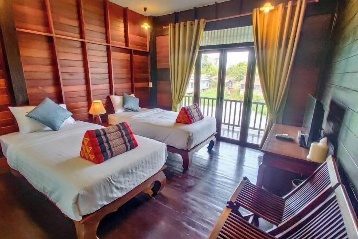 A room with two beds, a wooden floor, a balcony, and a TV.