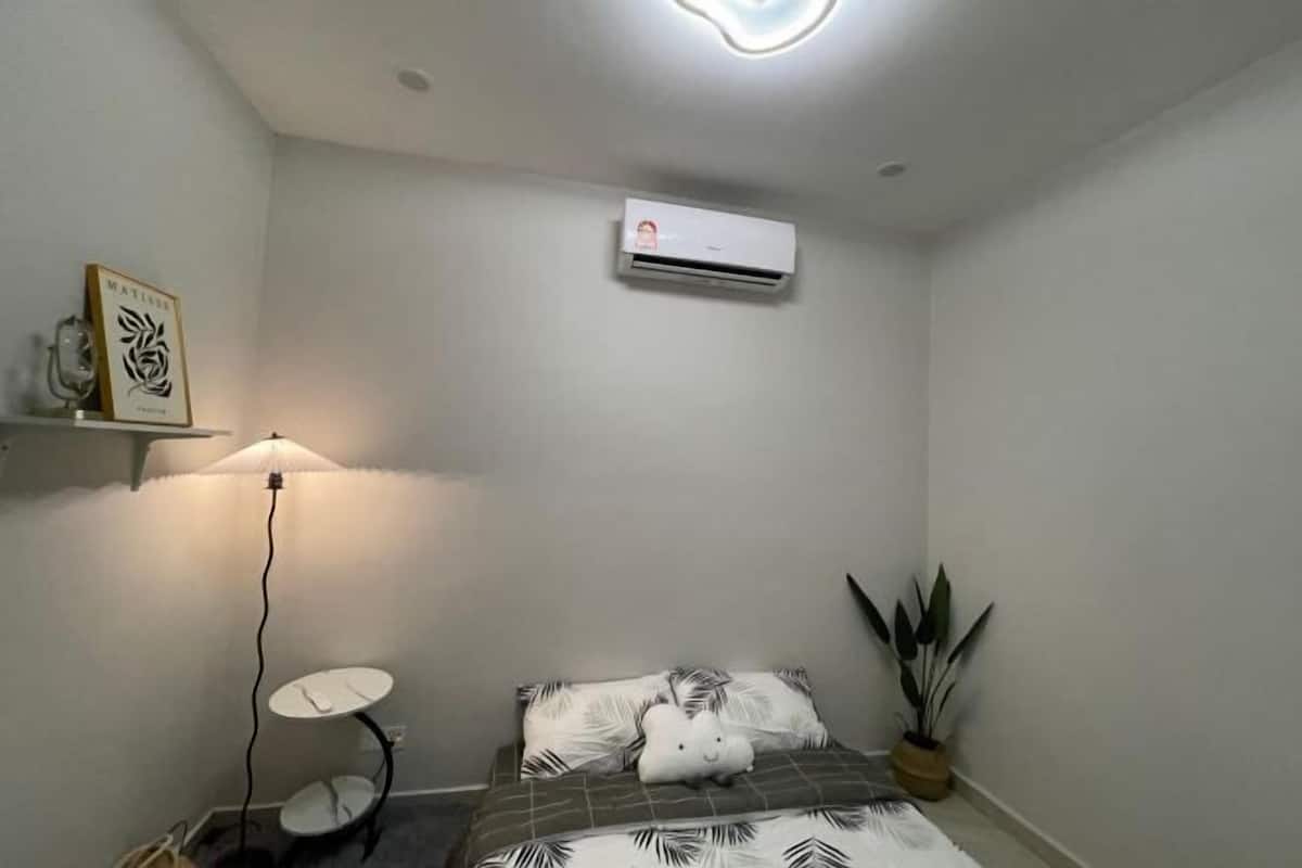 Une chambre à coucher comprenant un lit, un climatiseur, une lampe, une petite table et une plante en pot.