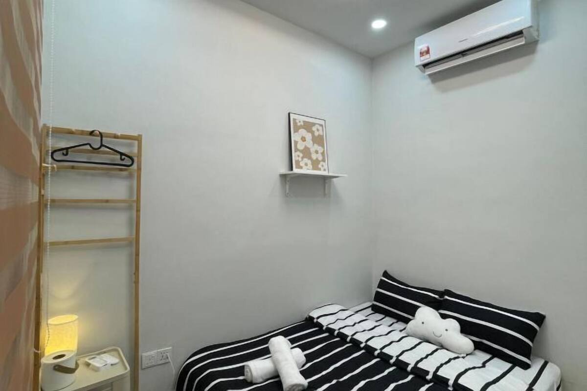 Une chambre à coucher avec un lit, une table de chevet avec une lampe, un climatiseur fixé au mur et une petite étagère avec un tableau.