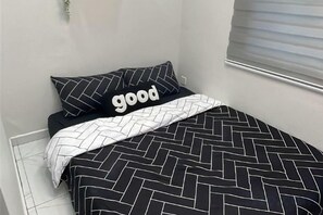 A bed with a black and white geometric patterned bedspread and a pillow with the word 'good' on it.