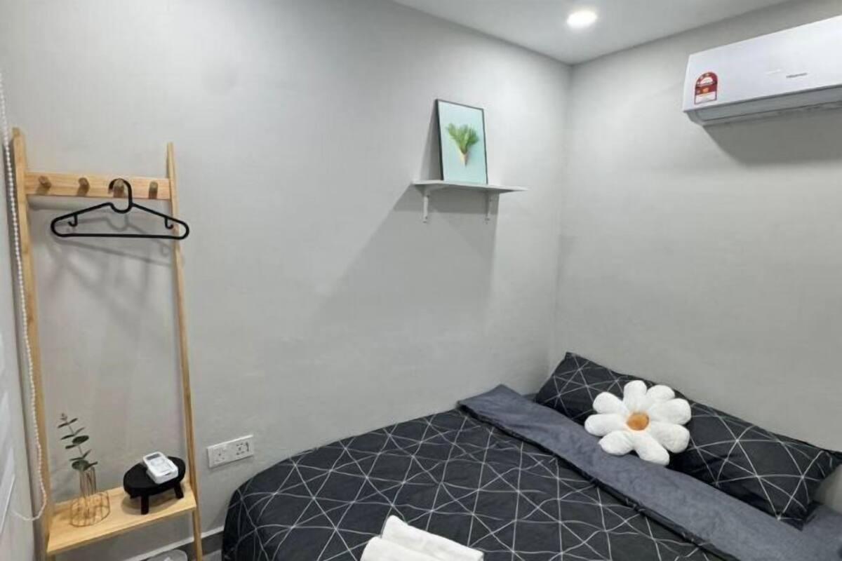 Une chambre à coucher comprenant un lit, une table de chevet, un porte-manteau mural, une étagère fixée au mur avec un tableau, et un appareil de climatisation.