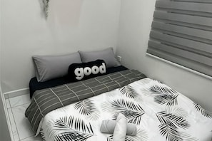 Et soveværelse med en seng, puder, et tæppe og en vægmonteret lampe.