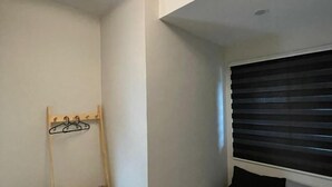 A room with a window with horizontal blinds, a coat rack with hangers, and a white wall.