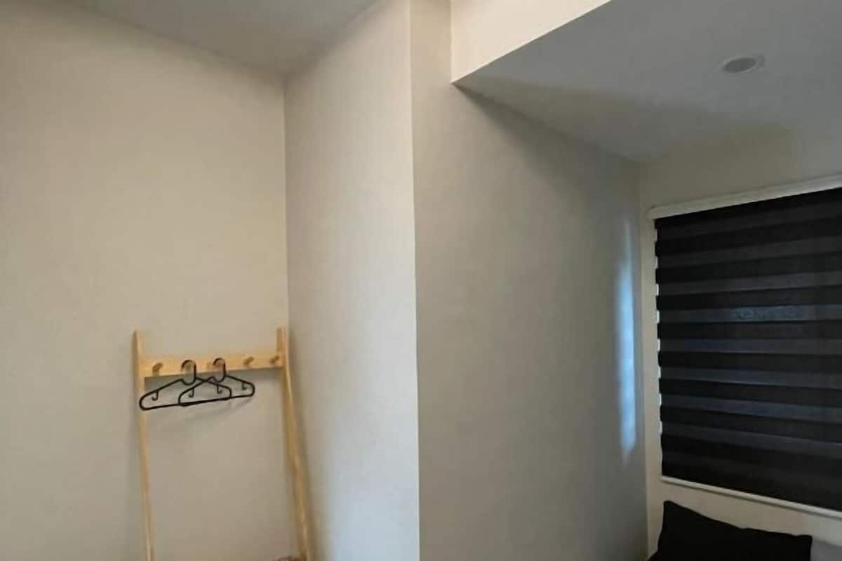 Une pièce avec une fenêtre dotée de stores horizontaux, un porte-manteau avec des cintres et un mur blanc.