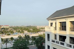 Un immeuble à plusieurs étages doté de balcons, d’un espace piscine agrémenté de palmiers, et offrant une vue sur une plage et des bâtiments situés au loin.