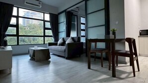 A modern living room with a sofa, a dining table, and chairs. There is a large window with curtains, an air conditioning unit, and a view of buildings and trees. - Peaceful JQ homestay (Kota Kinabalu)
