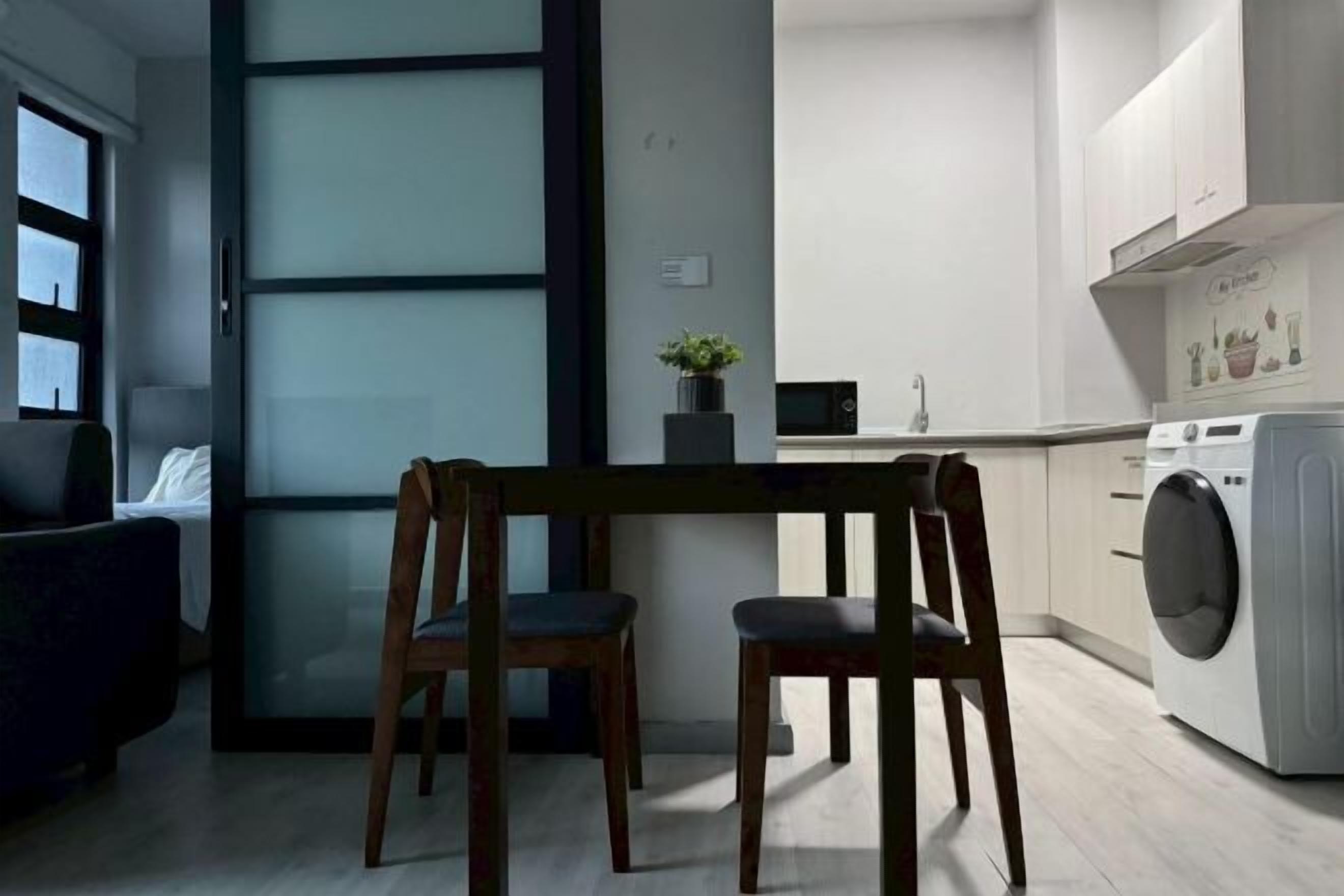 A modern kitchen with a built-in washing machine, a dining area with two chairs, and a view of the city through a large window.