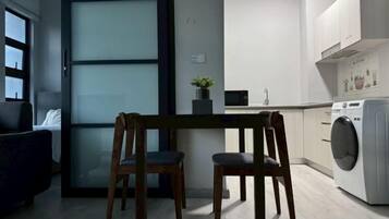 A modern kitchen with a built-in washing machine, a dining area with two chairs, and a view of the city through a large window.