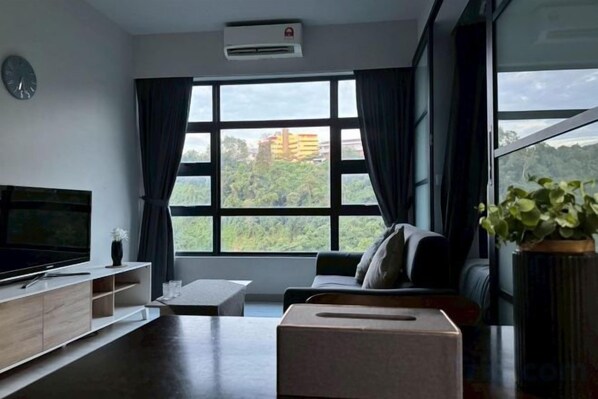 Una sala de estar moderna con un televisor de pantalla plana, un sofá, una mesa de centro y un ventanal con cortinas.