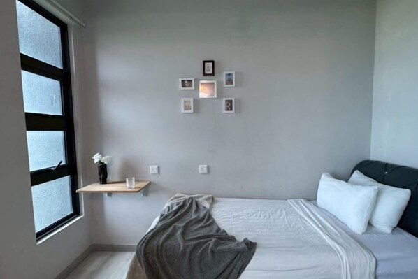 A bedroom with a bed, a window, and a wall-mounted shelf with a vase and a picture frame. - Peaceful JQ homestay (Kota Kinabalu)