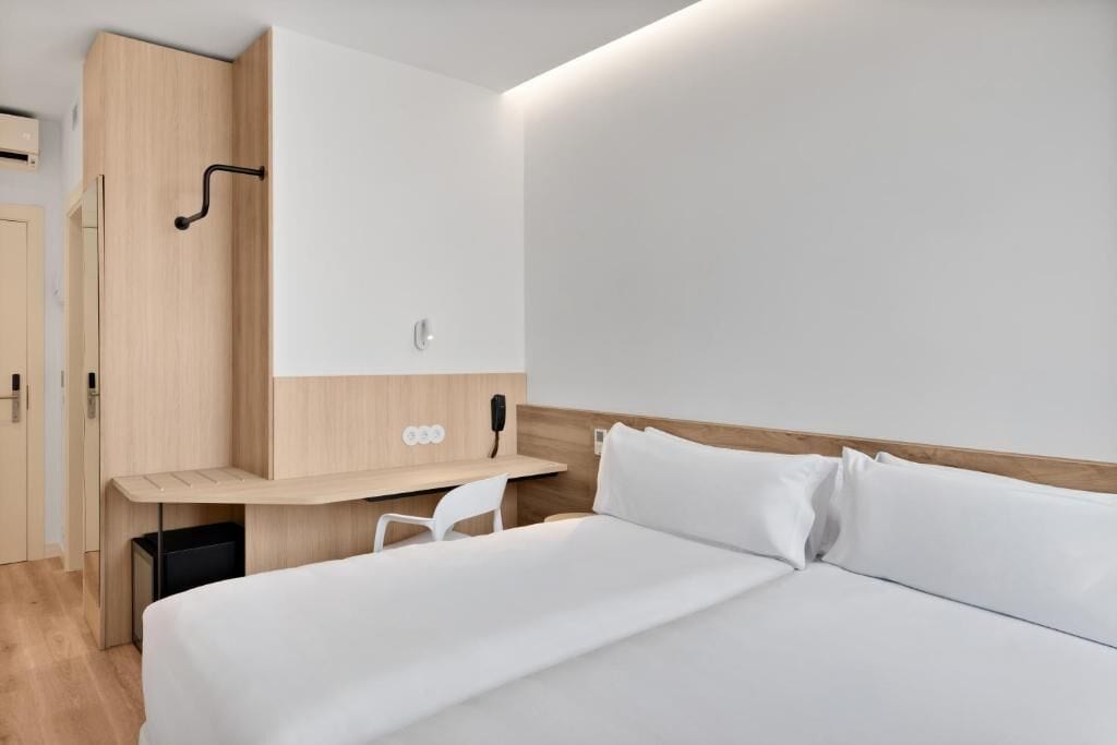 A modern hotel room with a bed, a desk, and a wardrobe.
