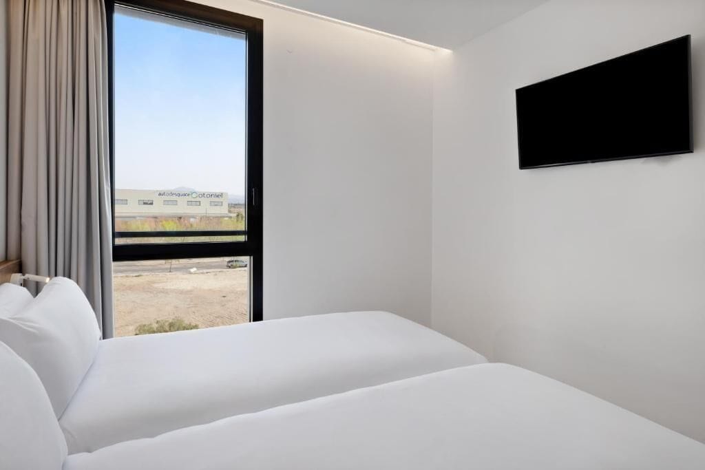 A hotel room with a large window, a bed, and a flat-screen TV mounted on the wall.